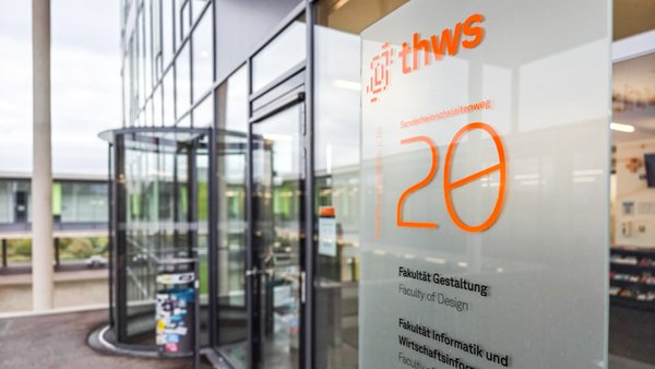 Entrance area of the faculty building. There is a glass panel with orange lettering next to the revolving door.