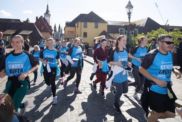 Runners at the Würzburg Marathon 2025 crossing a bridge, with historic buildings in the background.