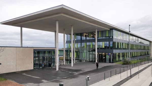 Exterior view of the faculty building. The modern building has a large concrete canopy and a glass façade with light green panels.